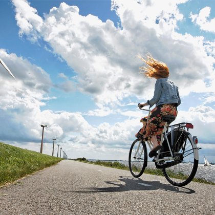 Young woman bicycle on a wind blown dike in Holland, wind turbines in the background