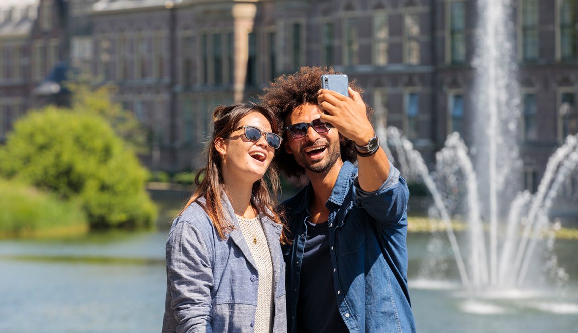 Cheerful young couple take selfies by the Hofvijver overlooking the Government Buildings