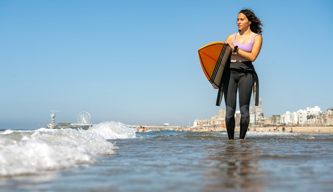 Surfer with board in swells with Scheveningen pier in the background
