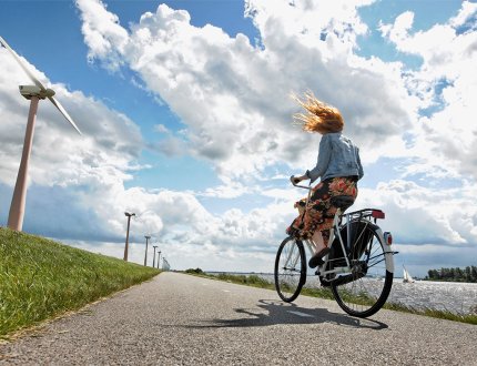 Young woman cycles on a windy road in the Netherlands, wind turbines in the background