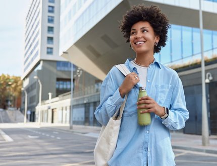 Happy curly haired woman carried fabric bag holds fresh water in bottle