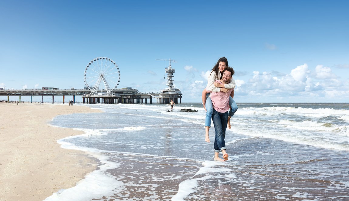 Couple enjoys on Scheveningen beach the pier with Ferris wheel in background
