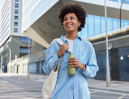 Happy curly haired woman carried fabric bag holds fresh water in bottle