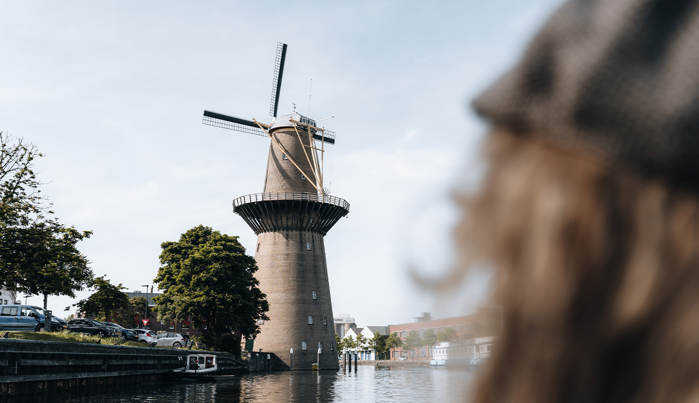 Over-the-shoulder view of a person gazing at 'De Nolet' windmill by a canal